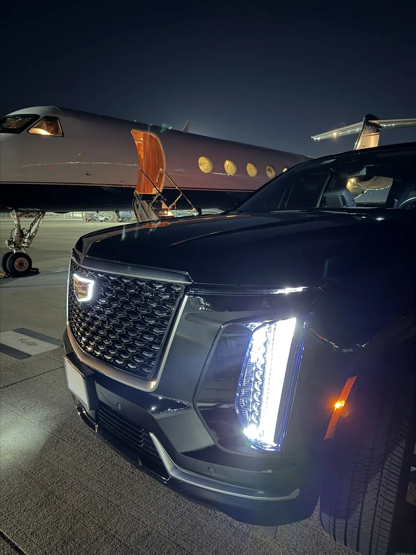Cadillac Escalade parked beside a private jet at night
