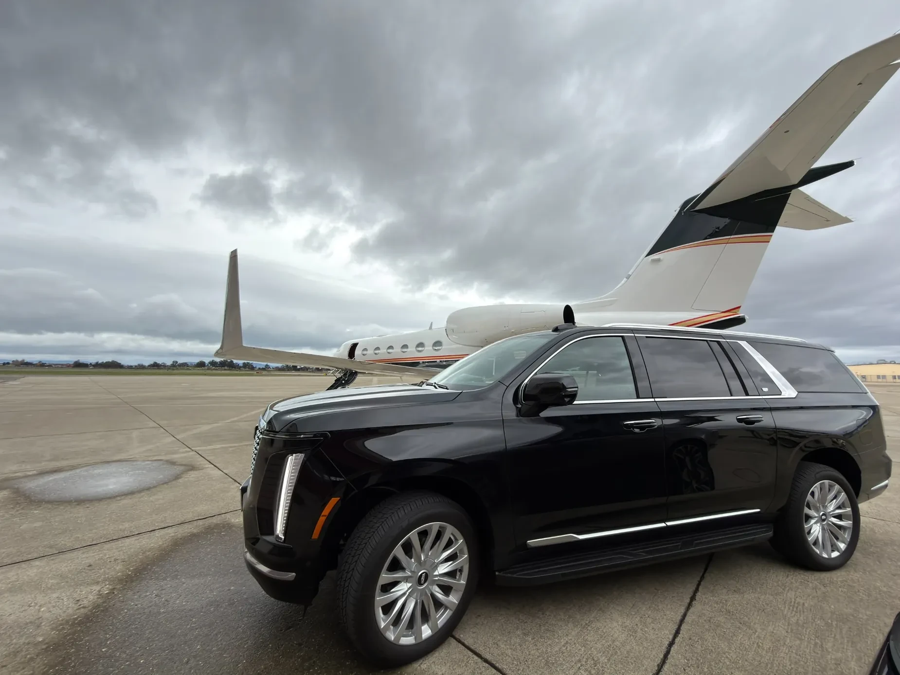 Black Cadillac Escalade parked beside a private jet